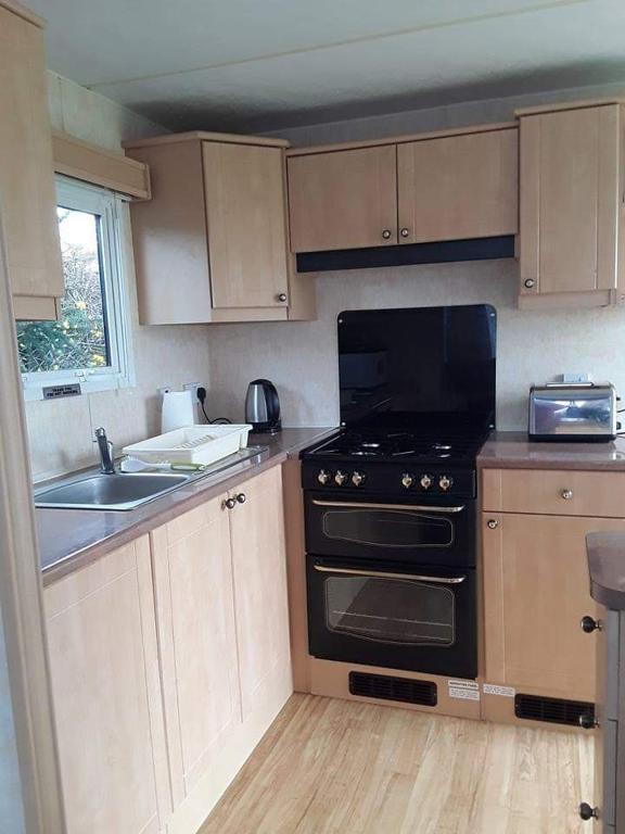 a small kitchen with a stove and a sink at Rhosfeillion Static Caravan in Llangefni