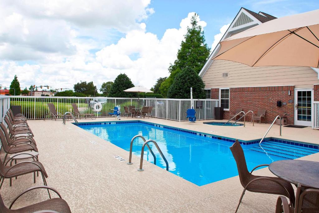 a swimming pool with chairs and a table and an umbrella at Residence Inn Baton Rouge Siegen in Baton Rouge