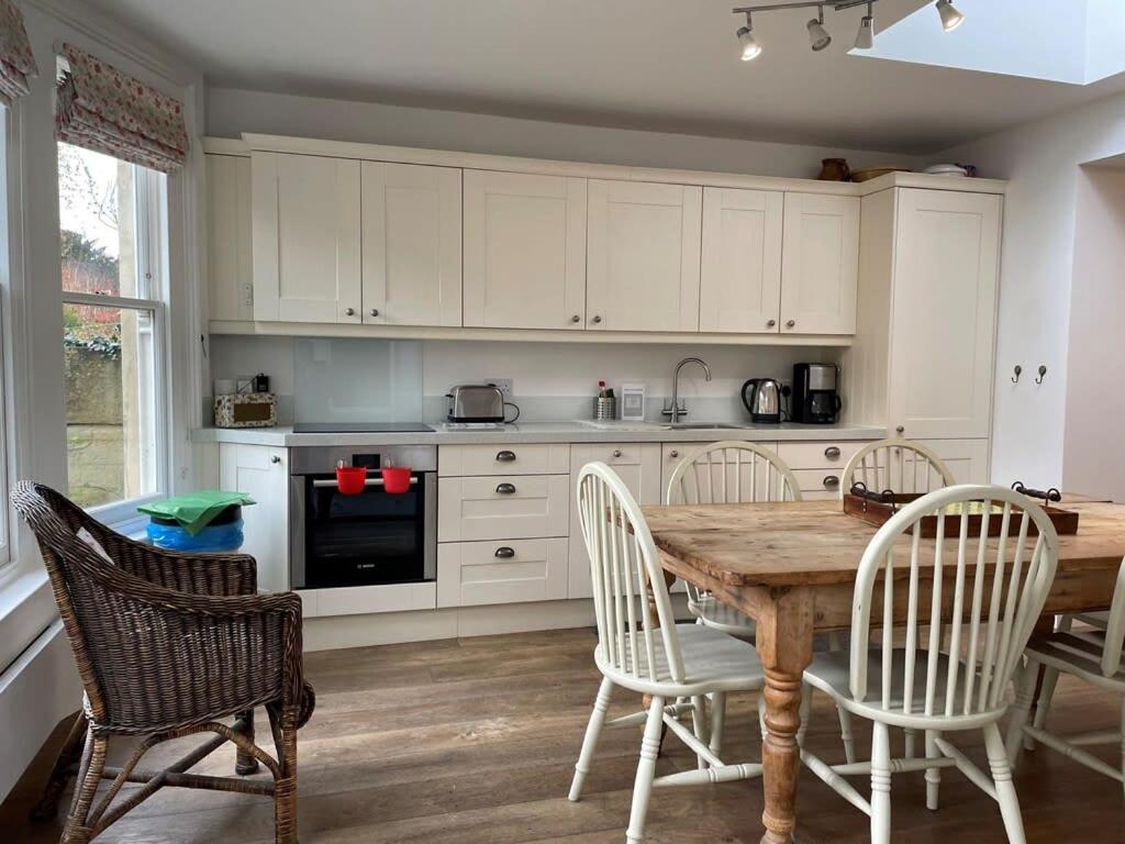 a kitchen with a wooden table and white cabinets at Beautiful 3 Bed Basement Flat With Garden in Bath