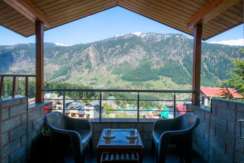 a table and chairs on a balcony with a view of mountains at Urban Monk- Highest Stay and Cafe of Manali in Manāli