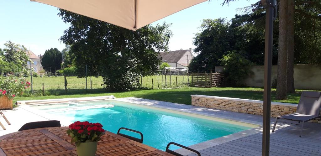 a swimming pool with a table and an umbrella at Le Clos des Roses in Chorey-lès-Beaune