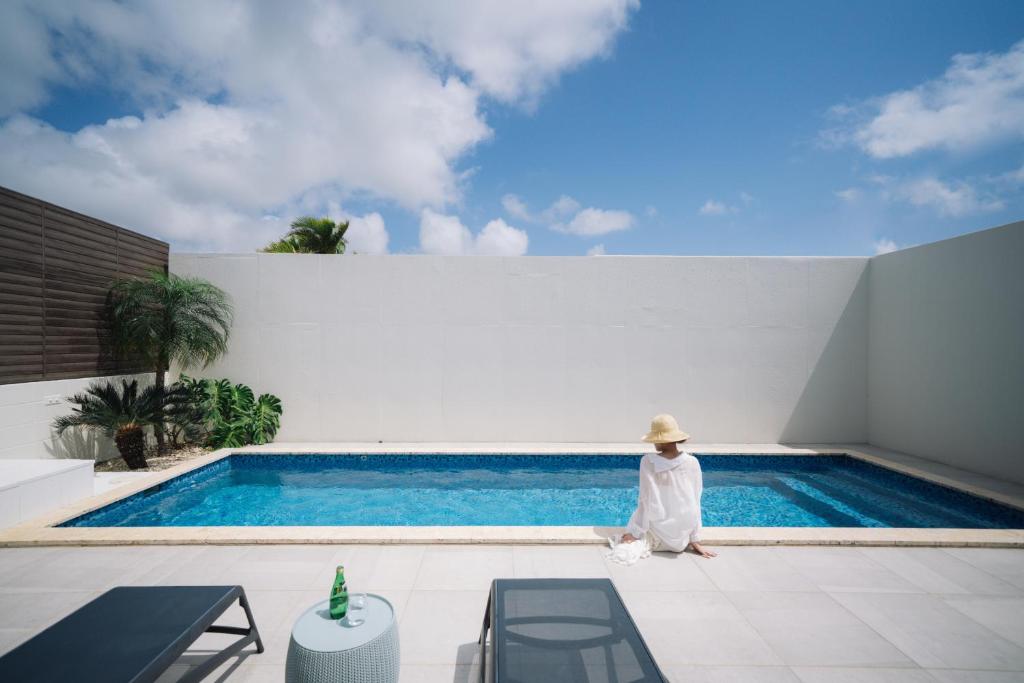 a person in a hat sitting next to a swimming pool at Villa Conte in Miyako Island