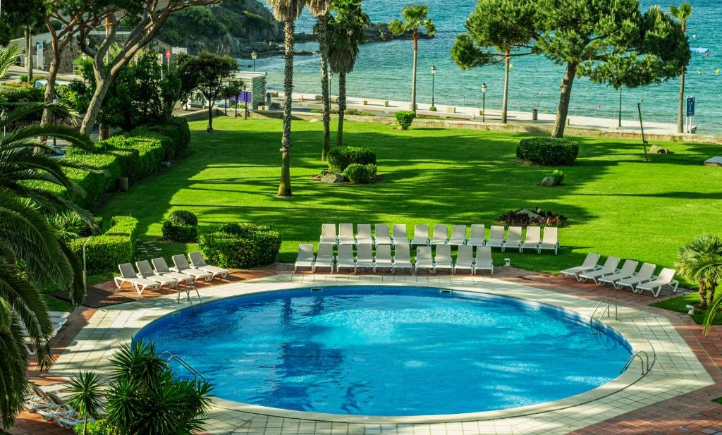 una piscina con sillas y el océano en el fondo en S'Agaró Hotel Spa & Wellness, en S'Agaró
