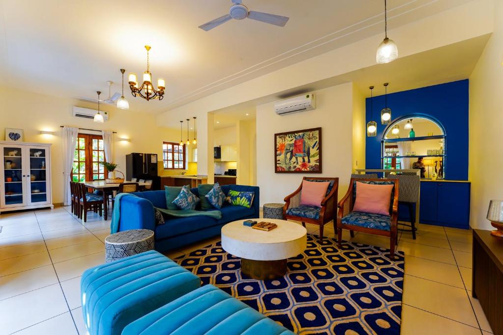 a living room with blue couches and a table at Elivaas Celest Luxe 4BHK Villa with Pvt Pool near Baga in Old Goa