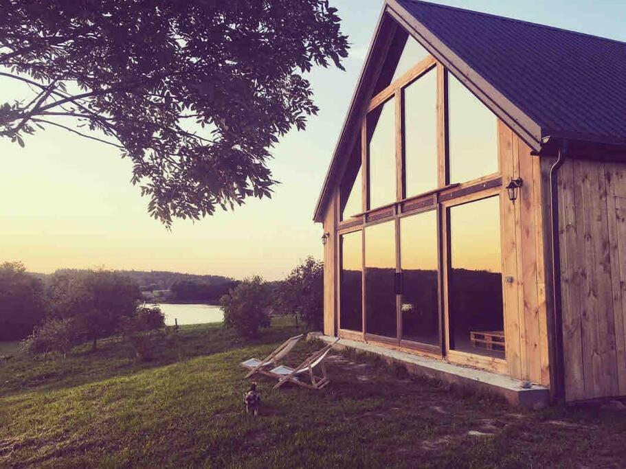 a small wooden building with glass windows on a field at Modern Barn Home & Sauna by the lake, przytulnastodola, Stodoła nad jeziorem na Mazurach in Ełk