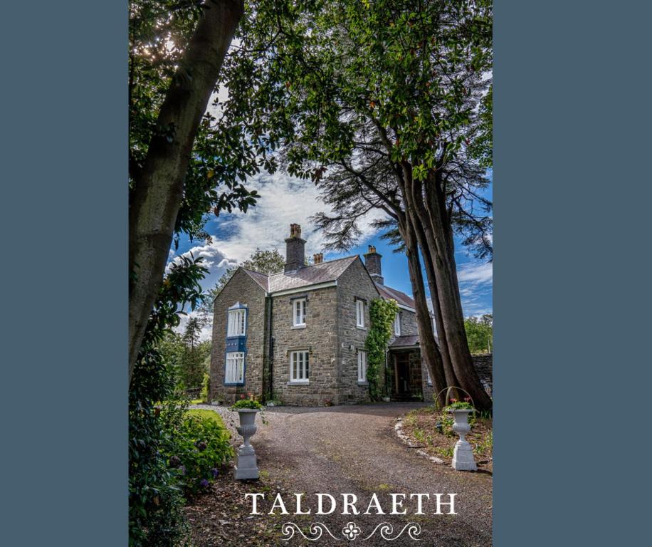 ein großes Steinhaus mit Bäumen davor in der Unterkunft Taldraeth - Old Vicarage Guest House in Penrhyndeudreath