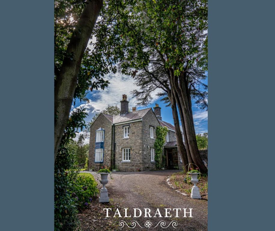 uma grande casa de pedra com árvores em frente em Taldraeth - Old Vicarage Guest House em Penrhyndeudreath