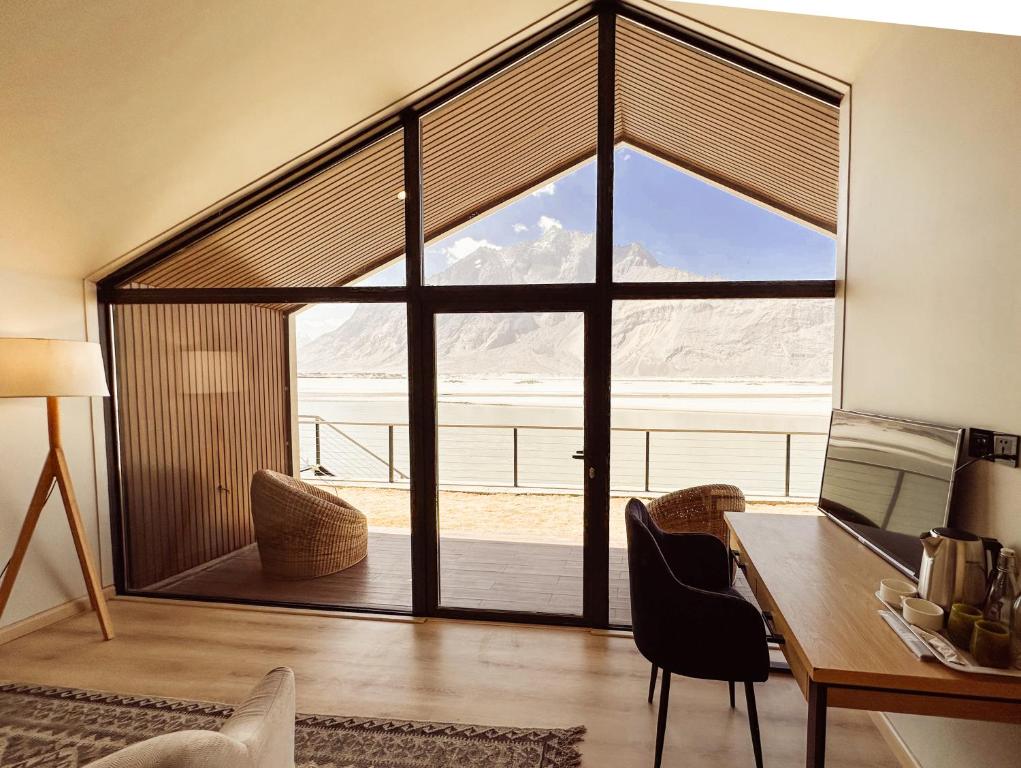 Cette chambre dispose d'un bureau et d'une grande fenêtre en verre. dans l'établissement Khoj Resorts, à Shigar