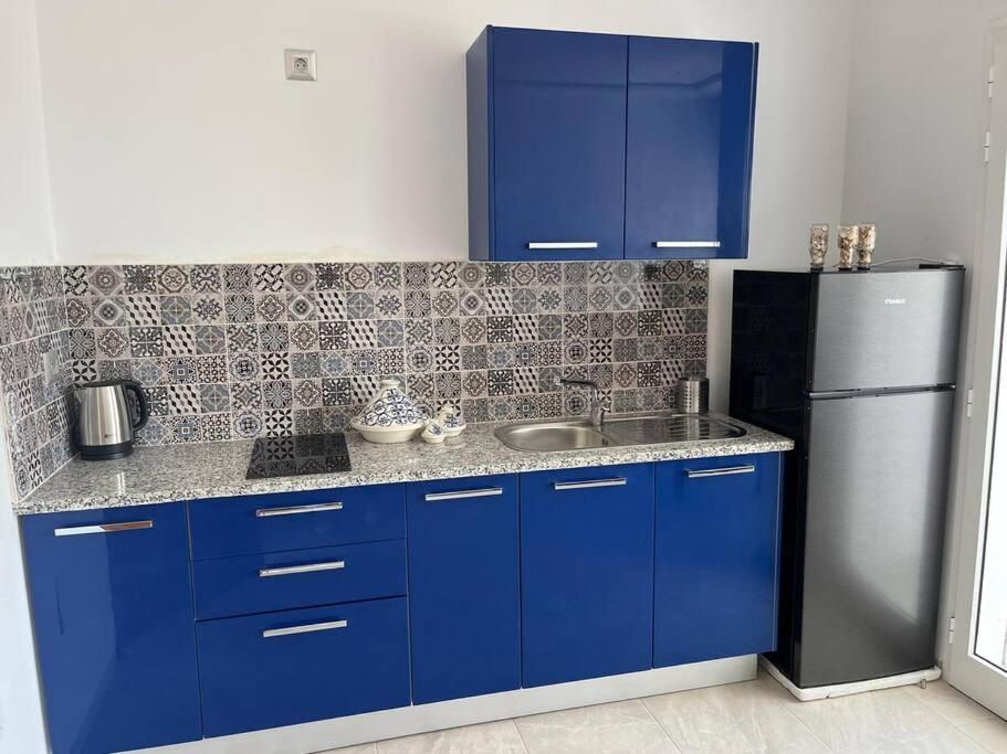 a kitchen with blue cabinets and a stainless steel refrigerator at Studio Bleu Cosy à Dar Lili Djerba in Mezraya