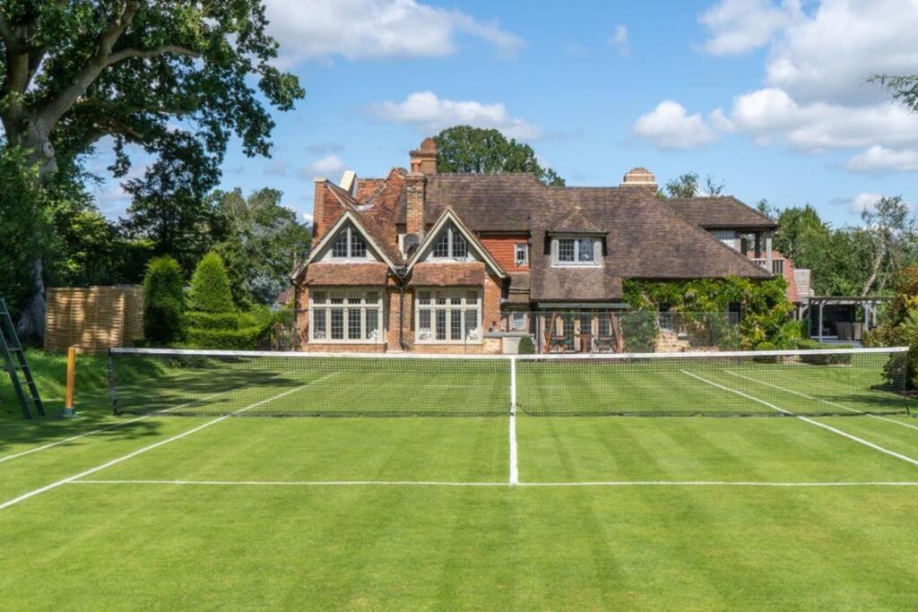 un campo da tennis di fronte a una grande casa di Lickfold Manor - Luxury home with swimming pool a Lurgashall