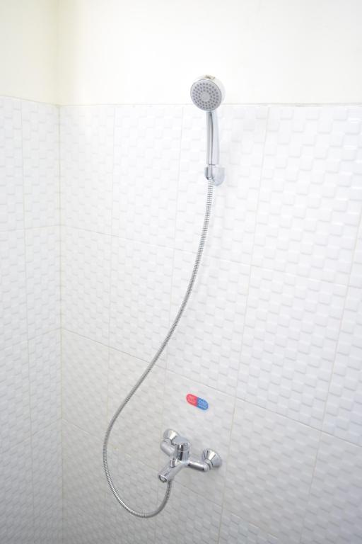 ジョグジャカルタにあるThe Cabin Hotel Ambasadorの白いタイル張りのバスルーム(シャワー、ホース付)
