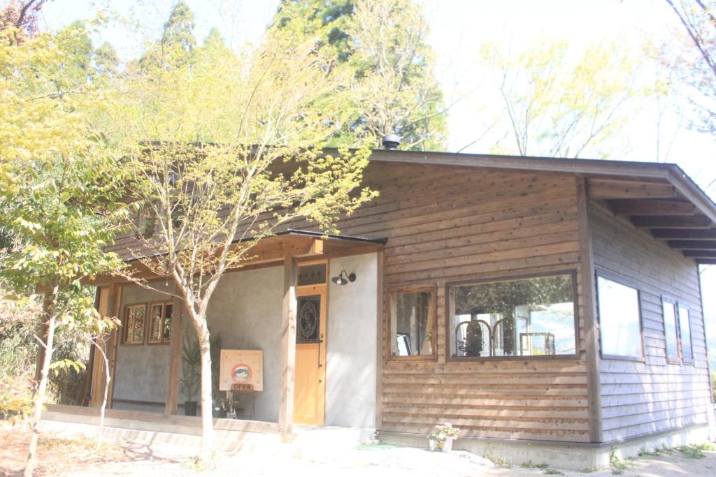 une petite maison en bois avec un arbre en face de celle-ci dans l'établissement 青い空と白い龍, à Minami Aso