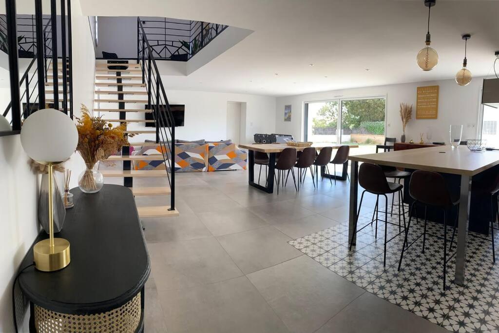 ein Wohnzimmer mit Tischen, Stühlen und einer Treppe in der Unterkunft Maison de 200 m2, récente à Noirmoutier en île in LʼHerbaudière