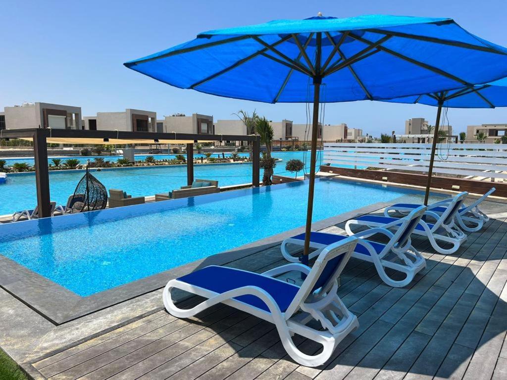 a group of chairs and an umbrella next to a swimming pool at Hacianda bay villa water villa in Sīdī ‘Abd ar Raḩmān