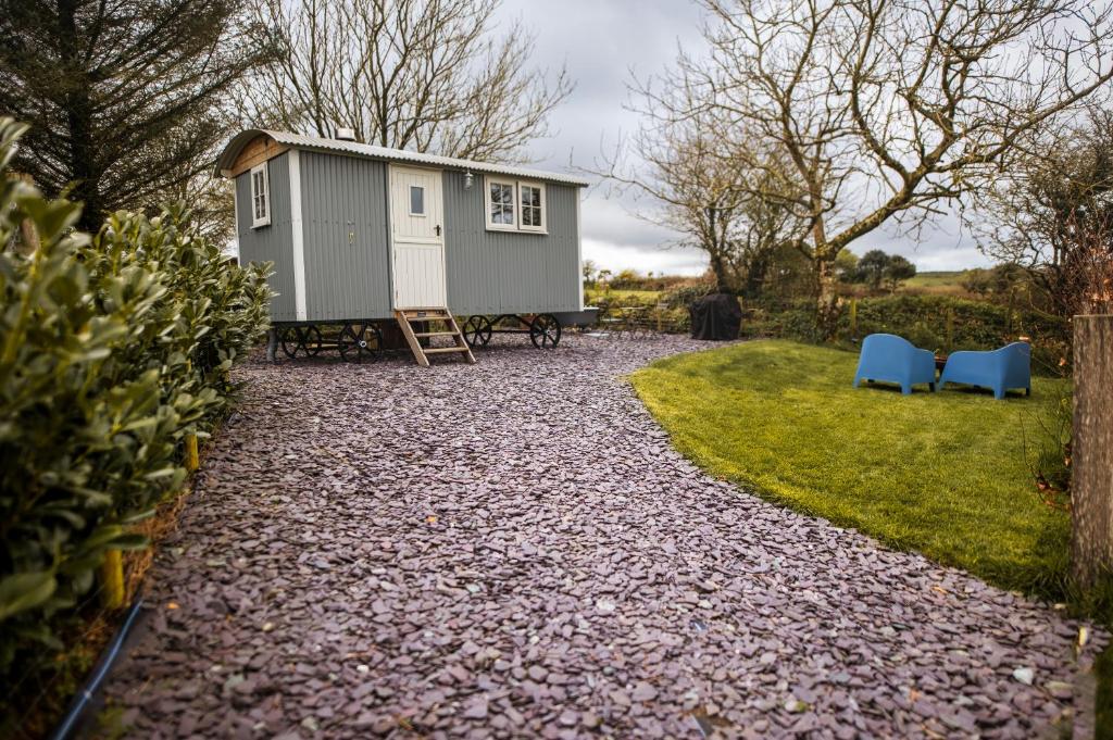 a tiny house in a yard with two blue chairs at Luxury Shepherd's Hut on Flower Farm with Outdoor Bath in Mid Cornwall in Truro