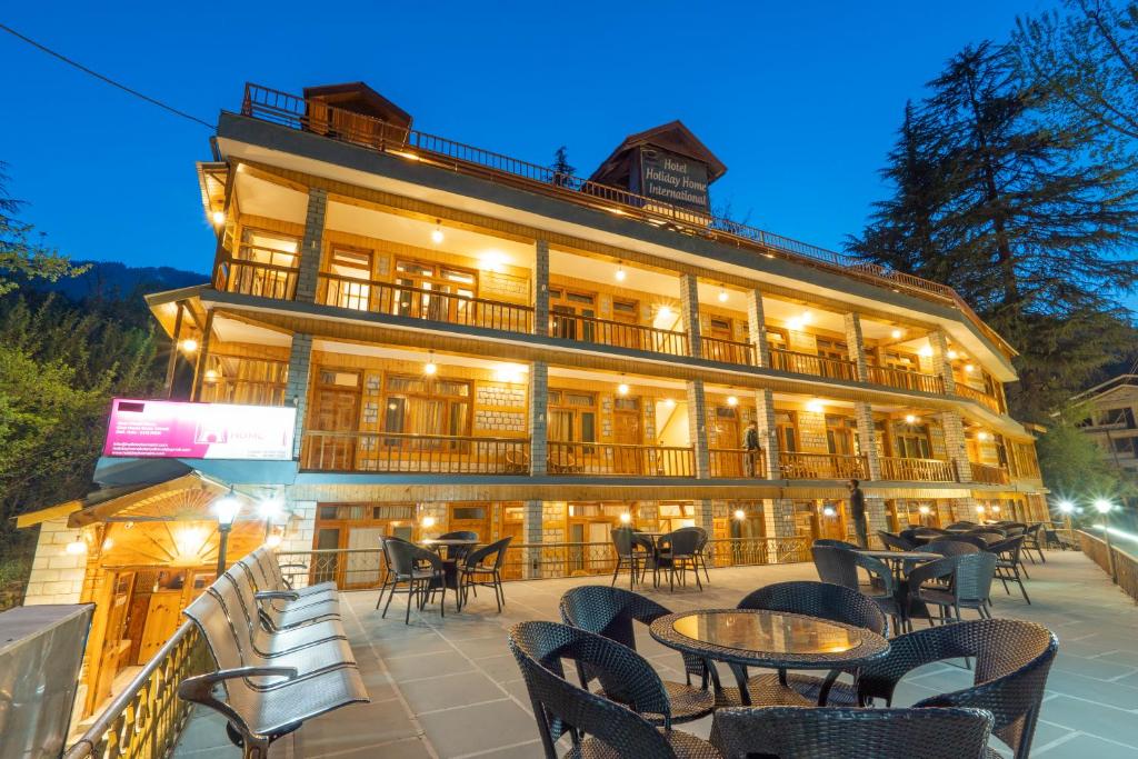 a hotel with tables and chairs in front of a building at Vivaan Stays -Holiday Home International in Manāli