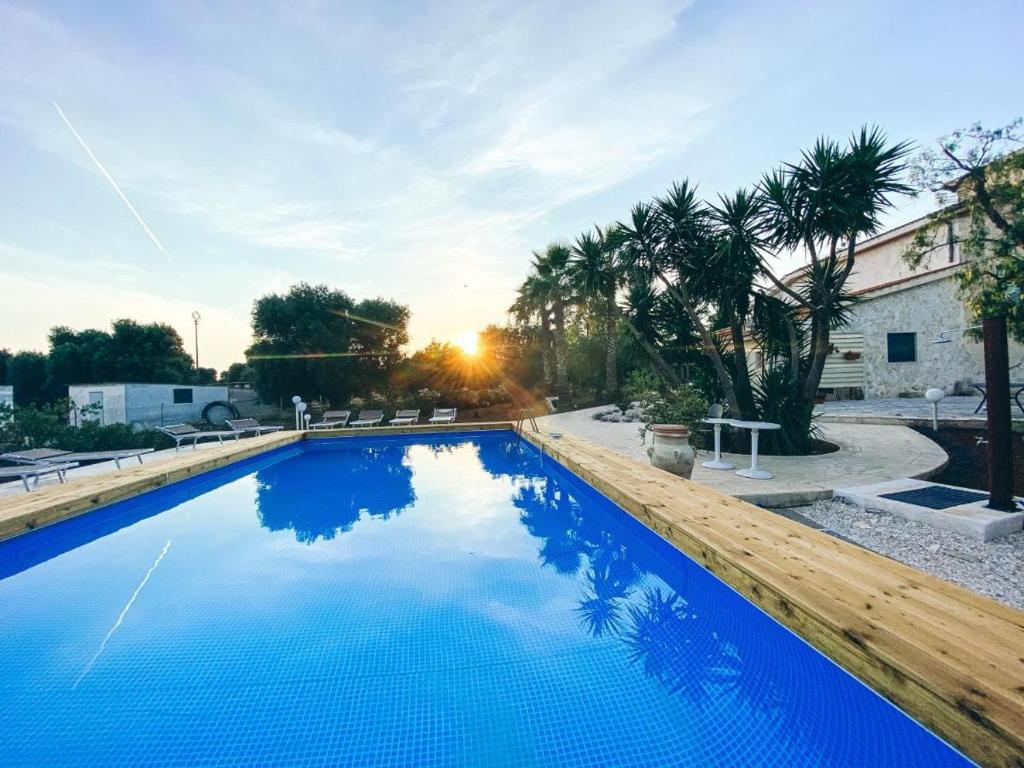 a blue swimming pool with a sunset in the background at La Maison One B&B in Carovigno