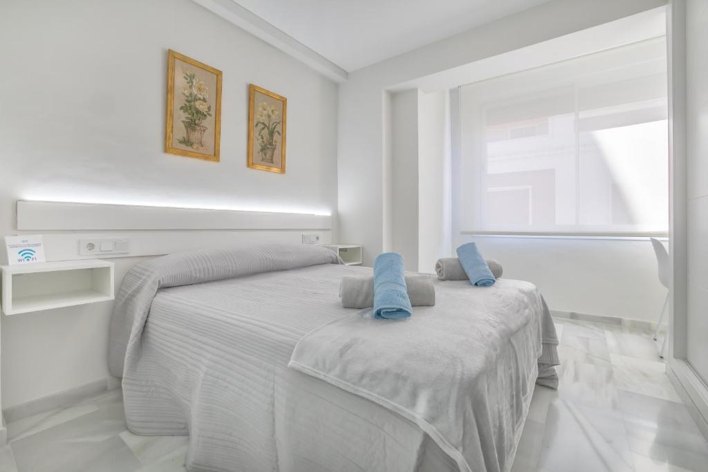 a white bedroom with a white bed with blue pillows at Apartamentos Haranas, parking incluido in Córdoba