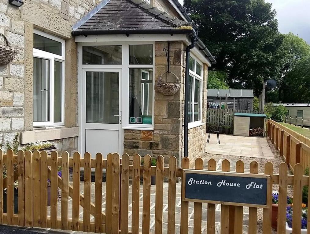 a small house with a wooden fence and a sign at Station House Self Catering, Catton in Hexham