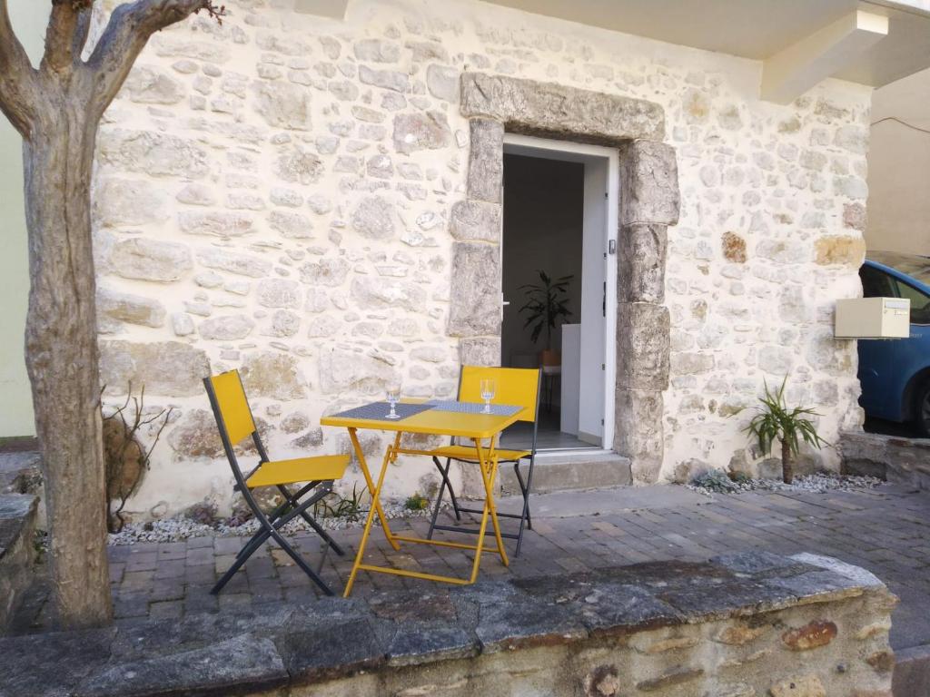 une table et des chaises jaunes à côté d'un mur en pierre dans l'établissement la placette, à Hérépian