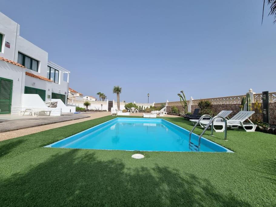 a large swimming pool with a green yard with chairs at Piscina y Relax junto al Mar! in Corralejo