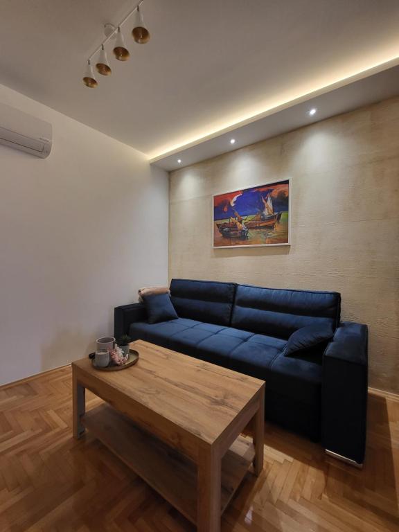 een woonkamer met een blauwe bank en een houten tafel bij Duga Apartmani 2 in Subotica