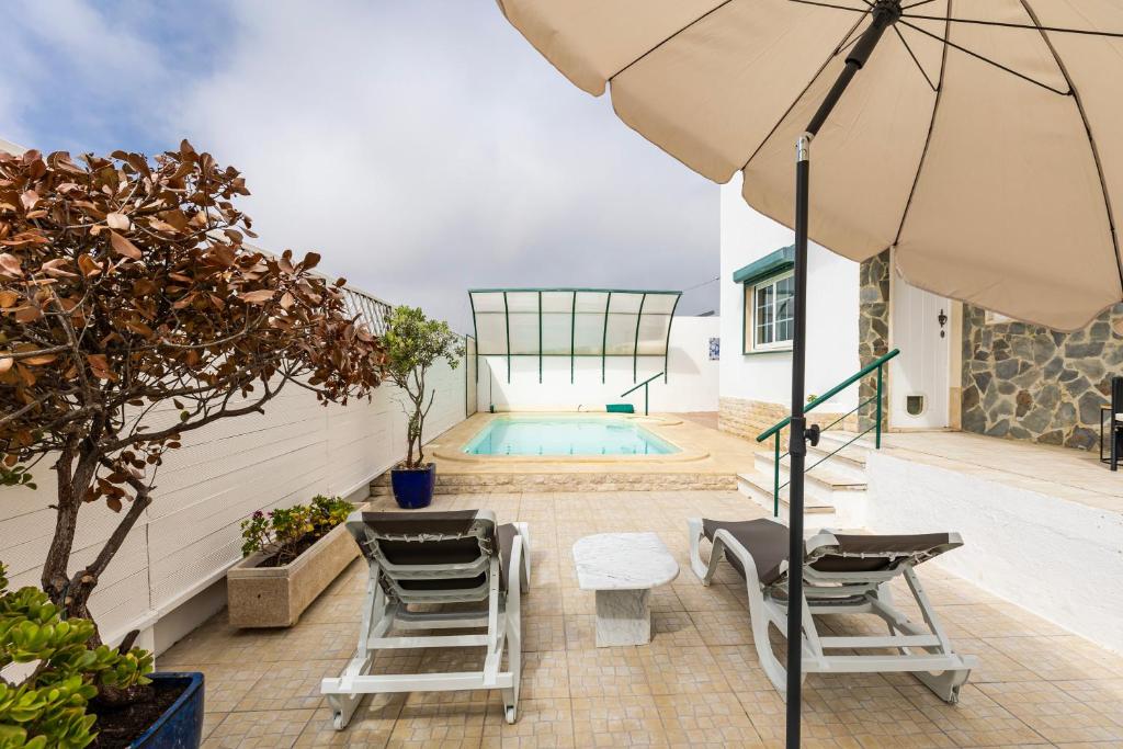 un patio avec des chaises et un parasol ainsi qu'une piscine dans l'établissement Spacious 3 bedroom house w/ swimming pool, à Ericeira