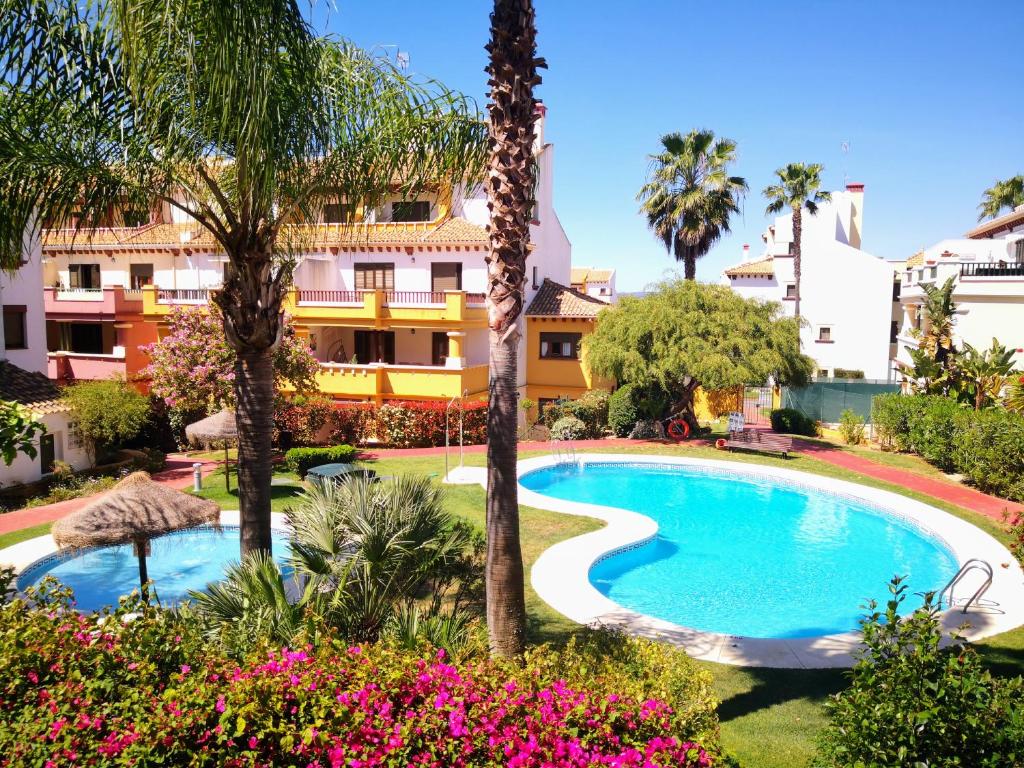 una piscina frente a un edificio con palmeras y flores en Marina Esuri Golf y Playa, en Ayamonte