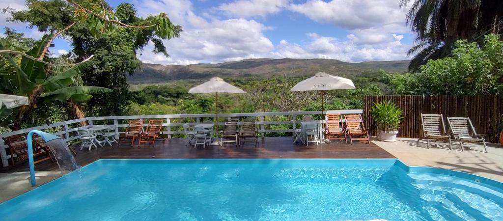 a pool with chairs and tables and a view of the mountains at Pousada Beira Rio Cipó in Serra do Cipo