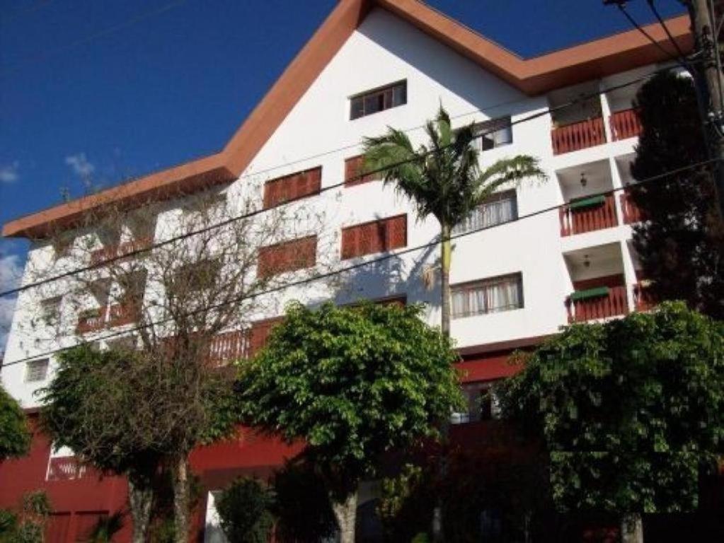 um edifício branco e vermelho com árvores em frente em Apartamento próximo aos principais pontos turísticos em Águas de Lindoia