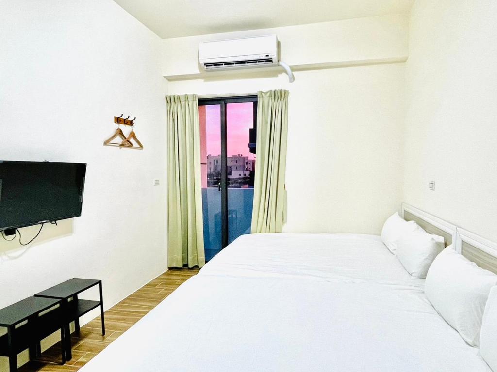 a white bedroom with a bed and a tv at Penghu Happy House in Magong