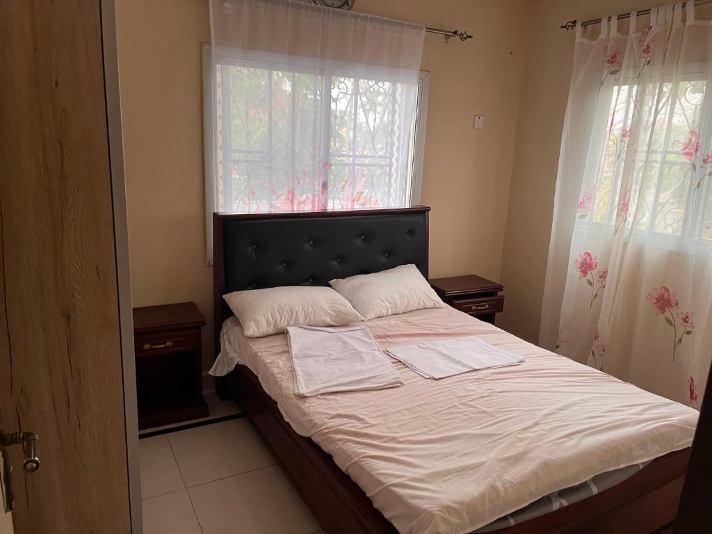 um quarto com uma cama com lençóis brancos e 2 janelas em B&Y Holiday Apartments em Brusubi
