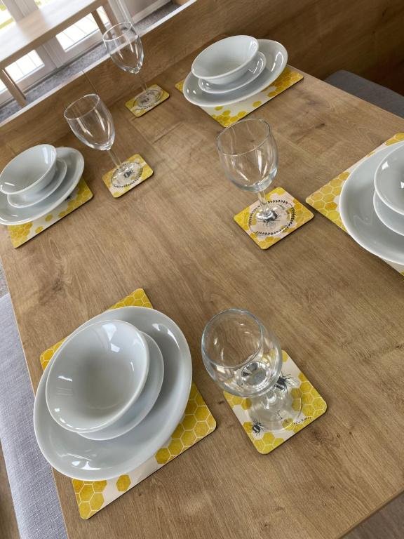 a wooden table with plates and wine glasses on it at Cosy holiday home at Romney Sands in New Romney