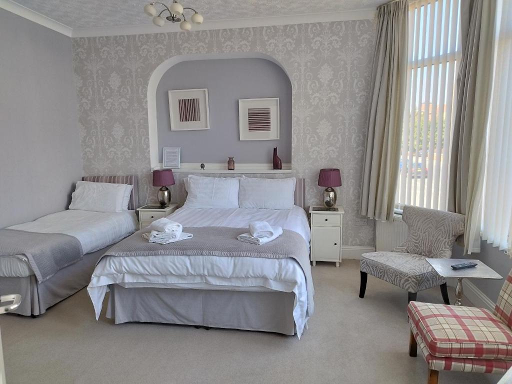 a white bedroom with two beds and a chair at The Monarch in Lytham St Annes