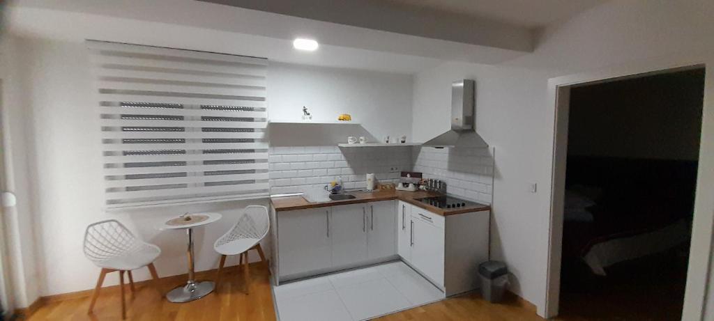 a small kitchen with white cabinets and white chairs at Apartman 222 in Brčko
