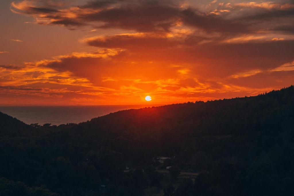 a sunset with the sun setting on a mountain at Amazigh Guincho Hostel & Suítes in Cascais
