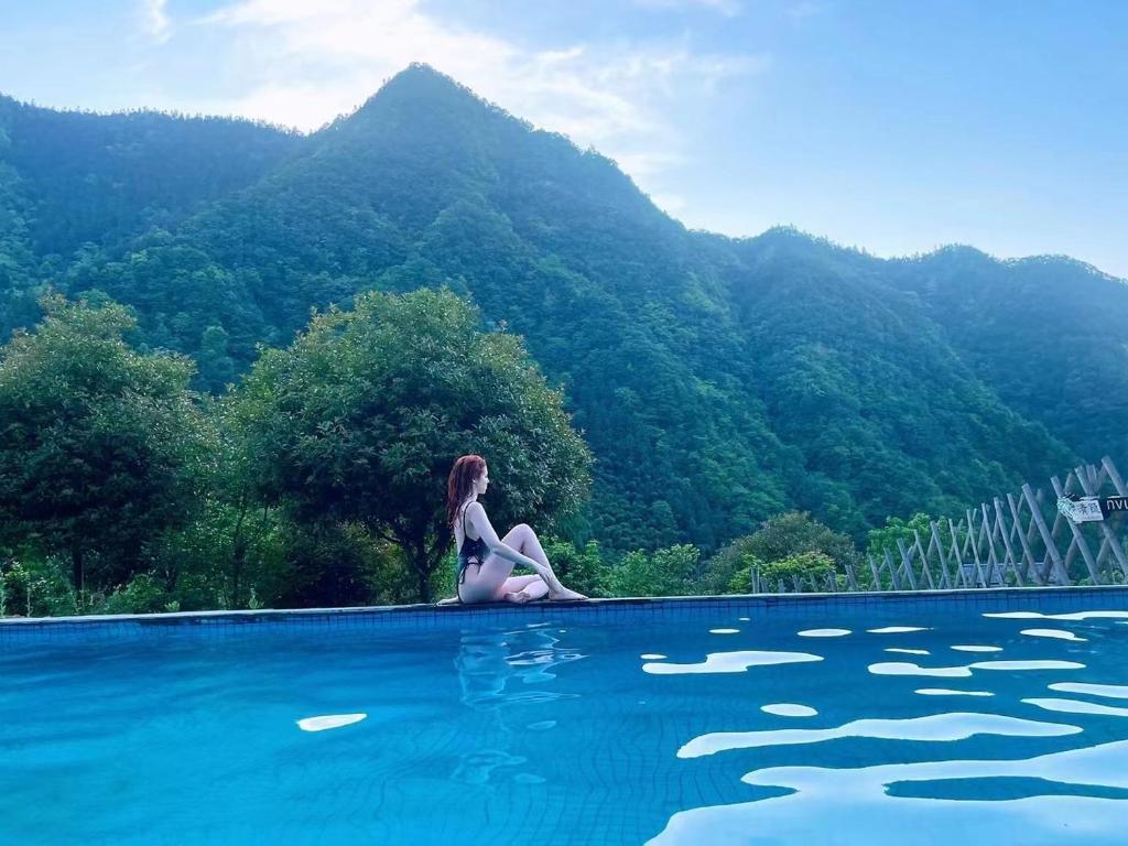 una donna seduta sul bordo di una piscina di Zhangjiajie National Park Nvue Resorts a Zhangjiajie