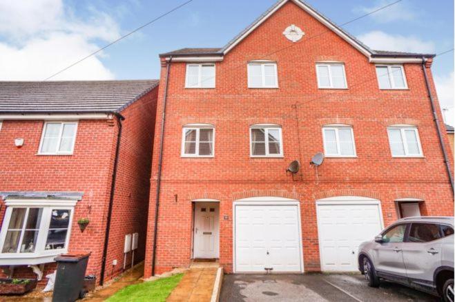 a red brick house with two white garage doors at Bulkington Lodge Coventry - Affordable Cosy Double & En-Suite Rooms in Bulkington