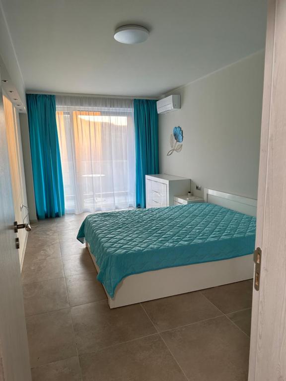 a bedroom with a bed with a green bedspread and blue curtains at ATEA APARTMENT KAVARNA in Kavarna