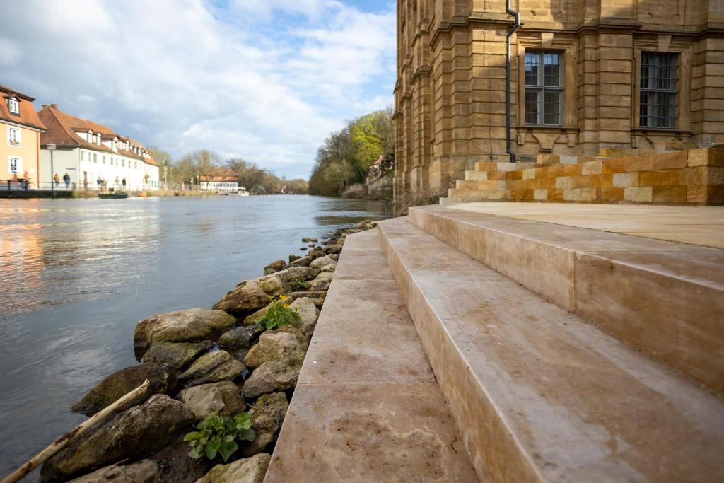 a river next to a building and some rocks at Concordia33 - Traumferienwohnung an der Regnitz in Bamberg