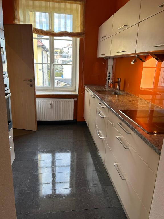 a kitchen with orange walls and white cabinets and a window at Große Ferienwohnung in Klagenfurt