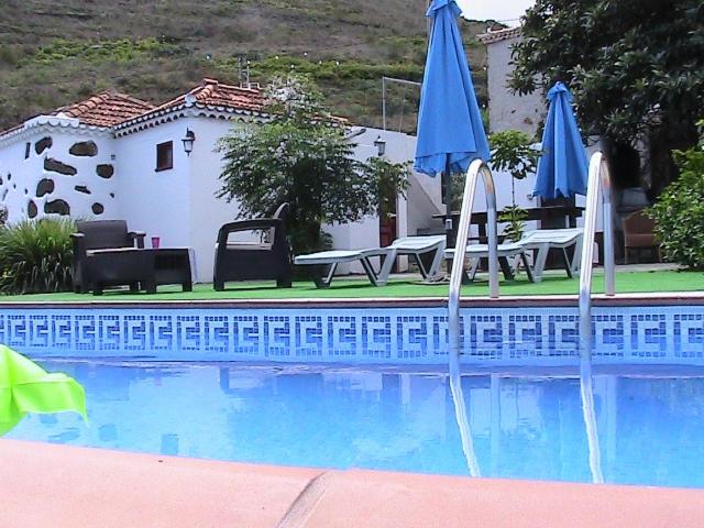 a swimming pool with two blue umbrellas and tables at Casa Rural Tía ilia in Puntallana