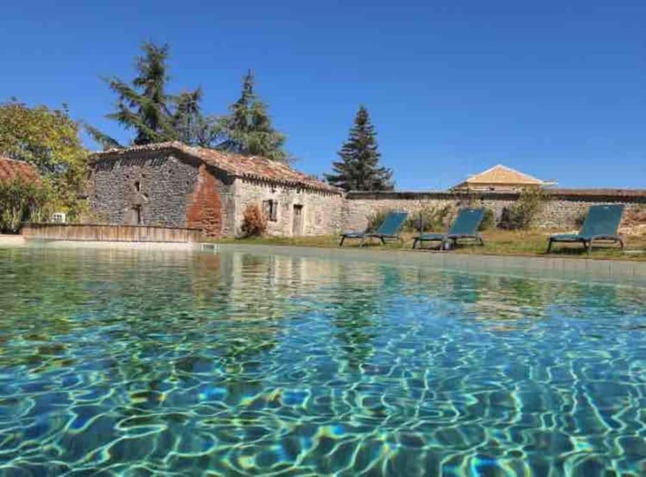 una piscina de agua con 2 sillas y un edificio en Chez Gaston, les gîtes de cazes, en Sérignac