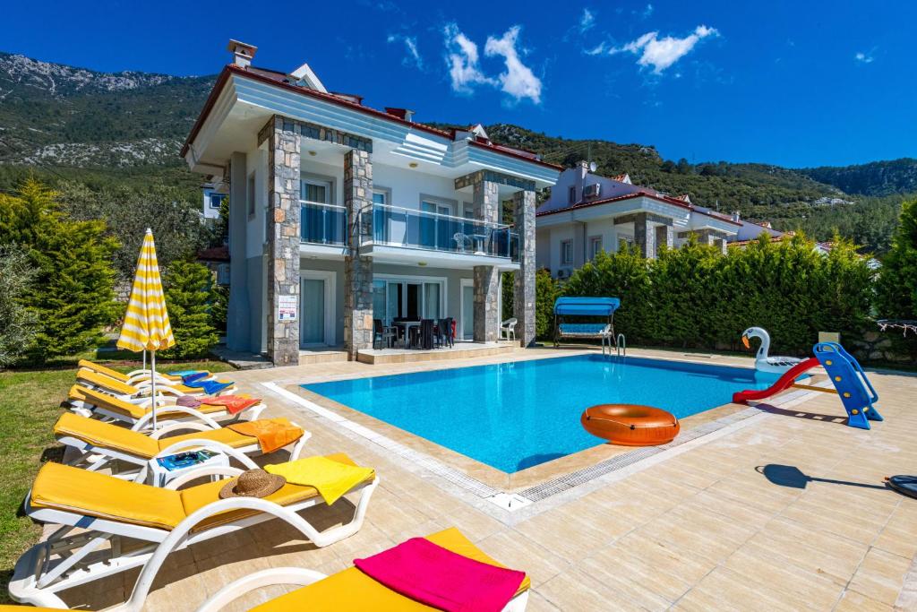 a villa with a swimming pool with chairs and a house at Yaşam Park Rena Villaları Ölüdeniz in Fethiye