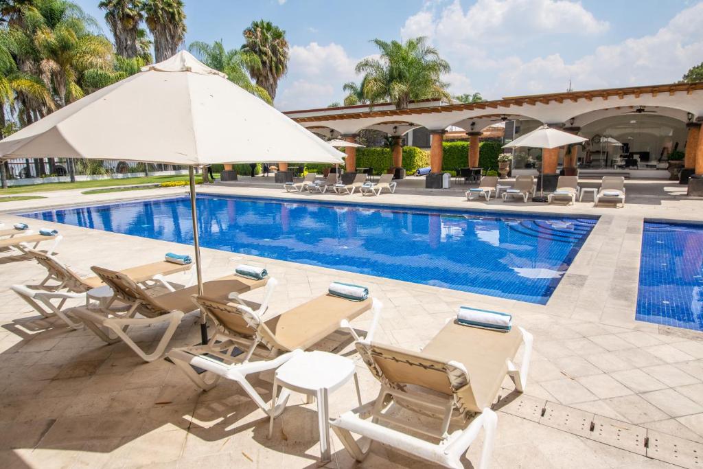 a swimming pool with chairs and an umbrella next to a pool at Hotel Hacienda la Venta in San Juan del Río