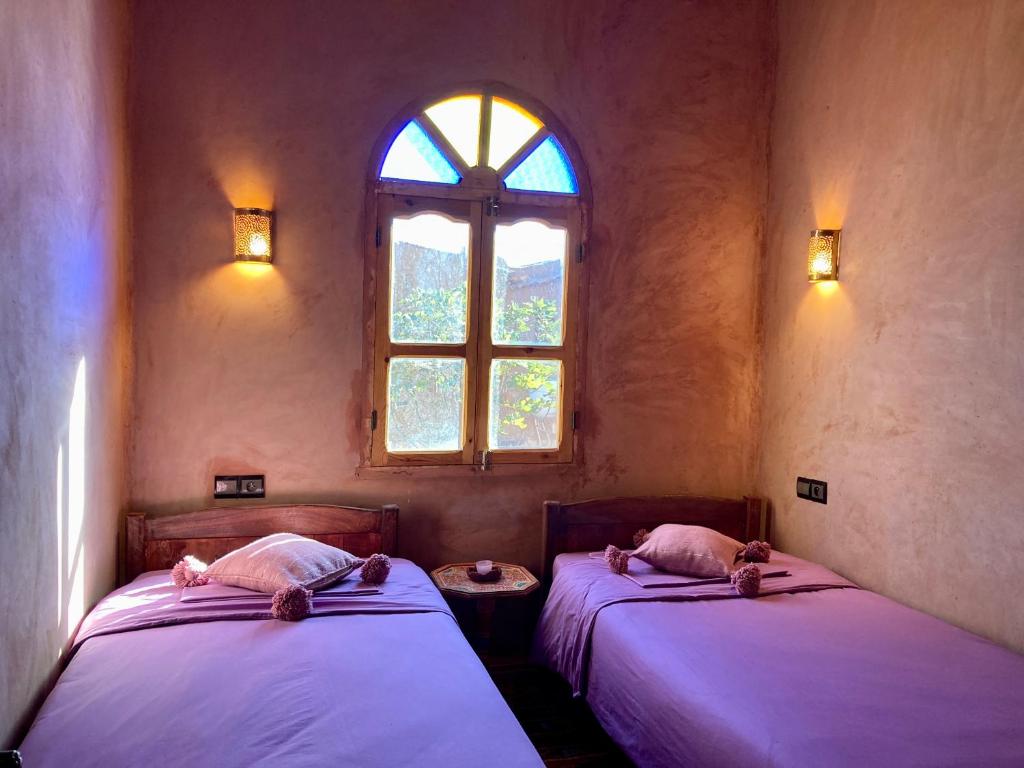 two beds in a room with a window at Riad Imuhar in Mhamid