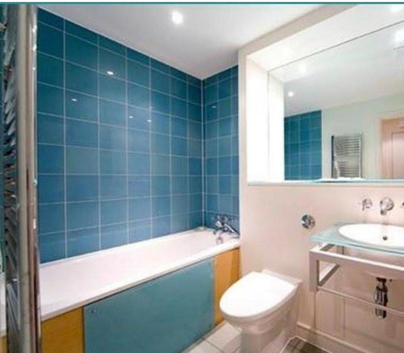 a blue tiled bathroom with a toilet and a sink at Juicey apartments in London