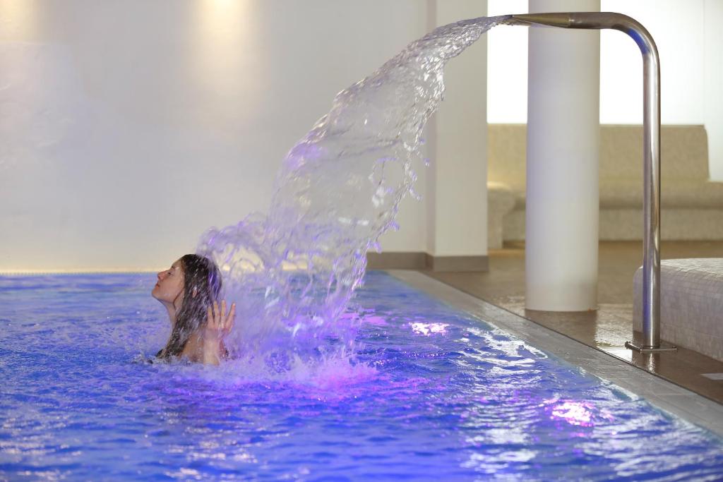 a woman in a swimming pool with a water fountain at Apartmány Engadin in Boží Dar