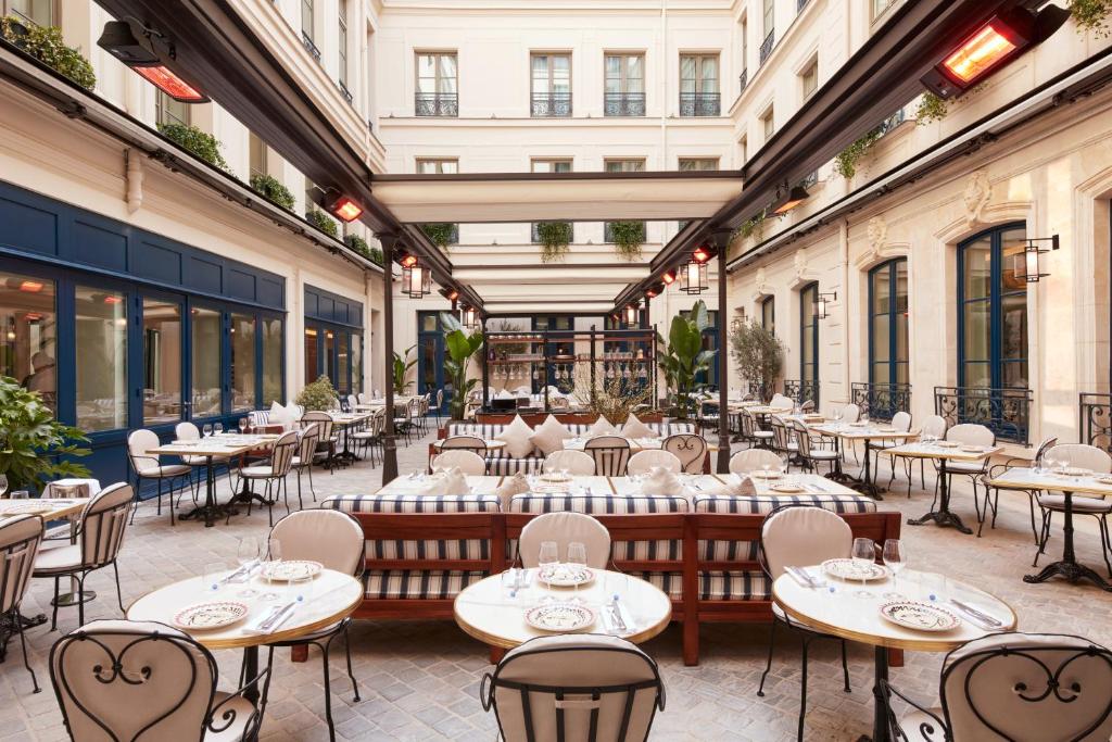 d'une terrasse avec des tables, des chaises et des fenêtres. dans l'établissement Maison Delano Paris, à Paris