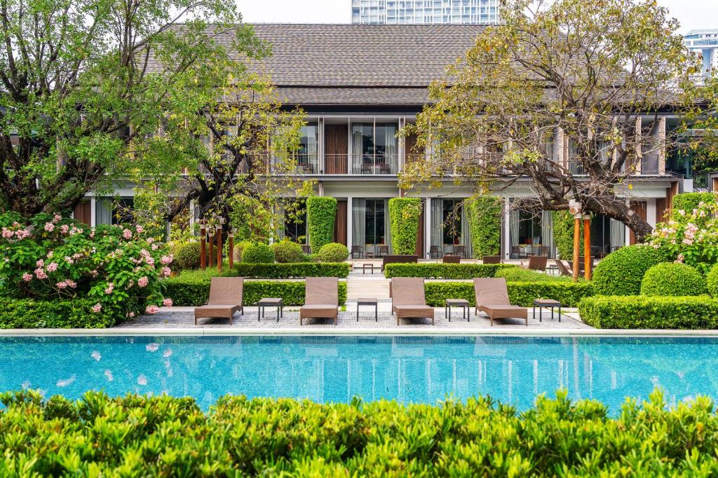a pool in front of a building with chairs and plants at Villa Deva Resort & Hotel Bangkok in Bangkok